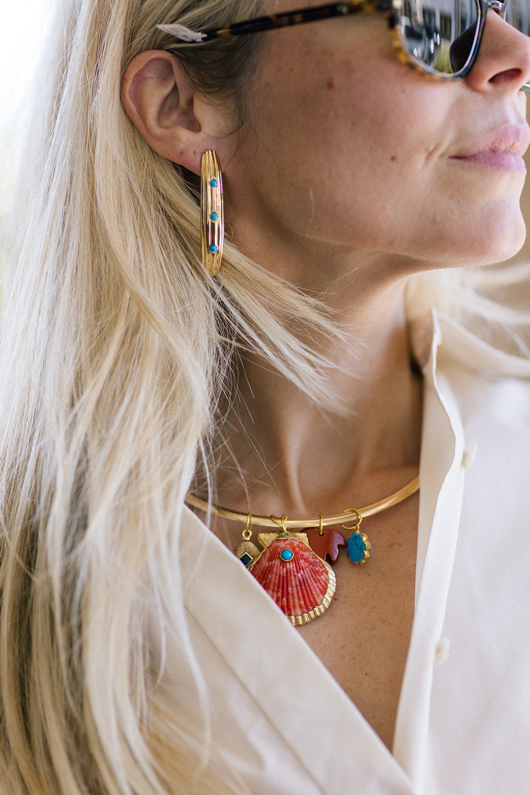 Close-up of a person wearing gold curved earrings and a necklace with colorful pendants.