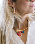 Close-up of a person wearing gold curved earrings and a necklace with colorful pendants.