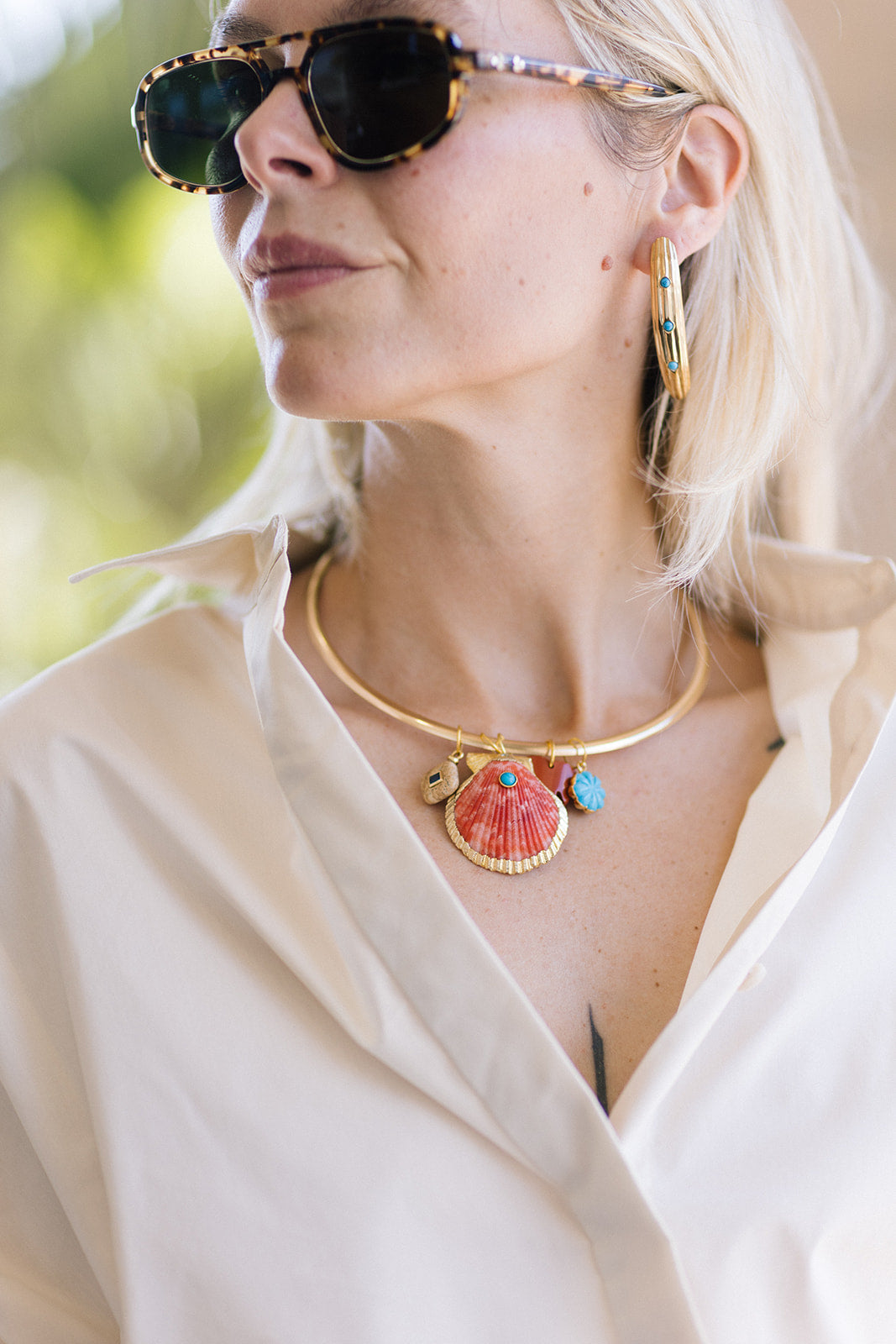 Woman wearing a gold necklace with seashell and starfish charms, sunglasses, and Nicolette 2" Earrings.