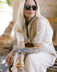 Woman with tattoos wearing sunglasses and a white outfit, sitting outdoors.