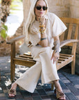 Woman in a white outfit sitting on a wooden bench outdoors with Sydney Rope Woven Block Heel