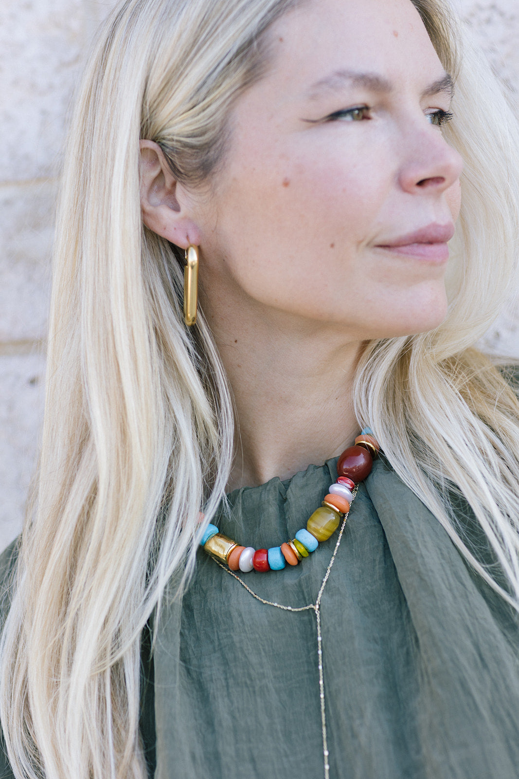 Woman wearing a colorful beaded necklace and gold hoop earrings against a neutral background