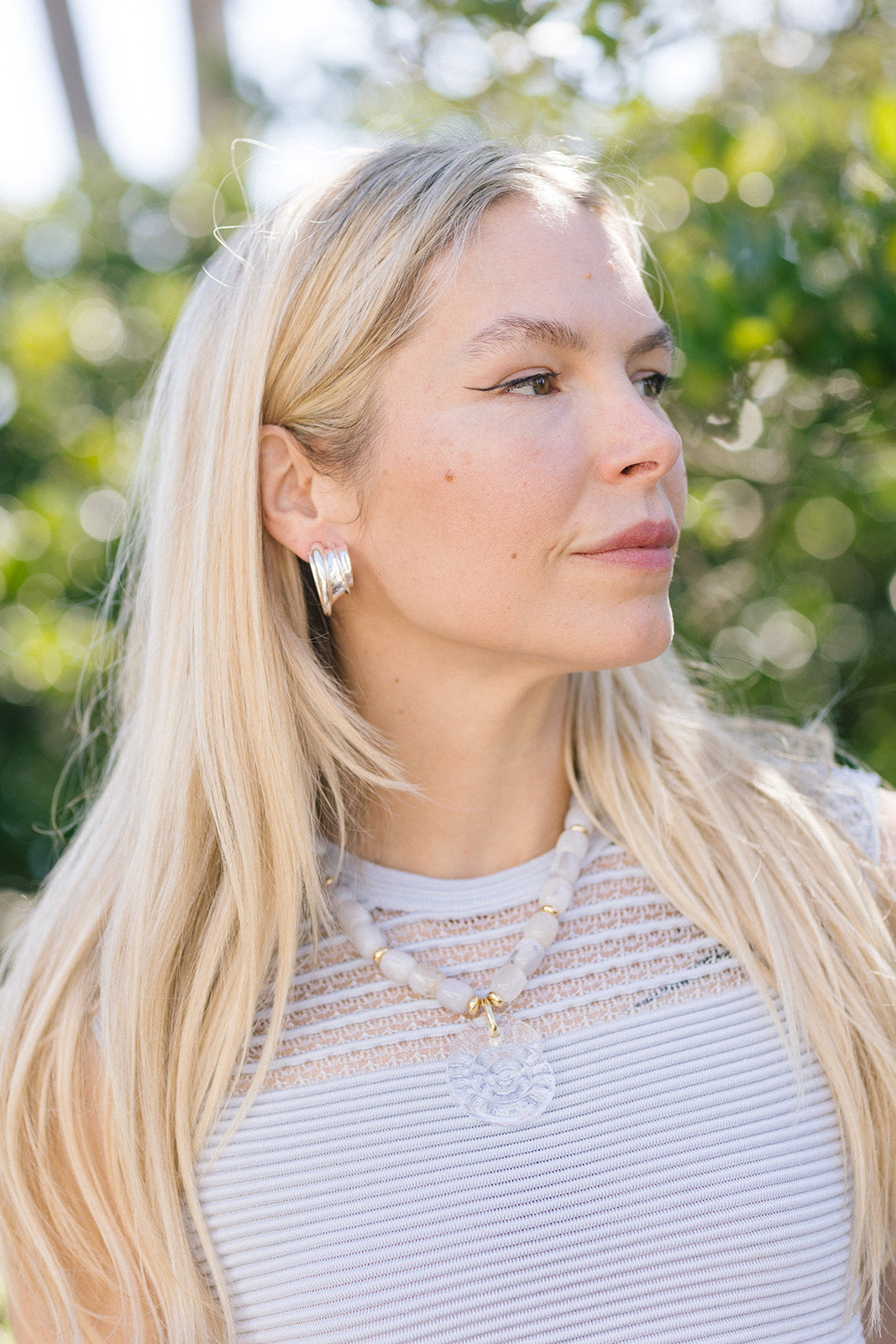 Woman with long blonde hair wearing a necklace and Leona Hoops Silver outdoors