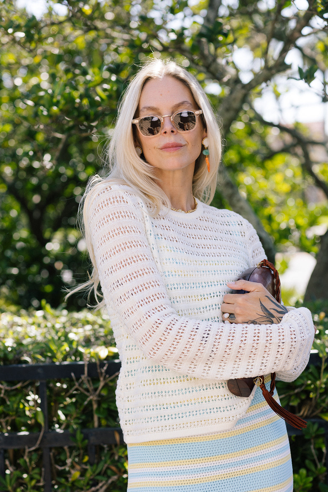 Woman wearing a white crochet top and striped skirt outdoors with greenery in the background