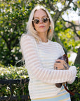 Woman wearing a white crochet top and striped skirt outdoors with greenery in the background