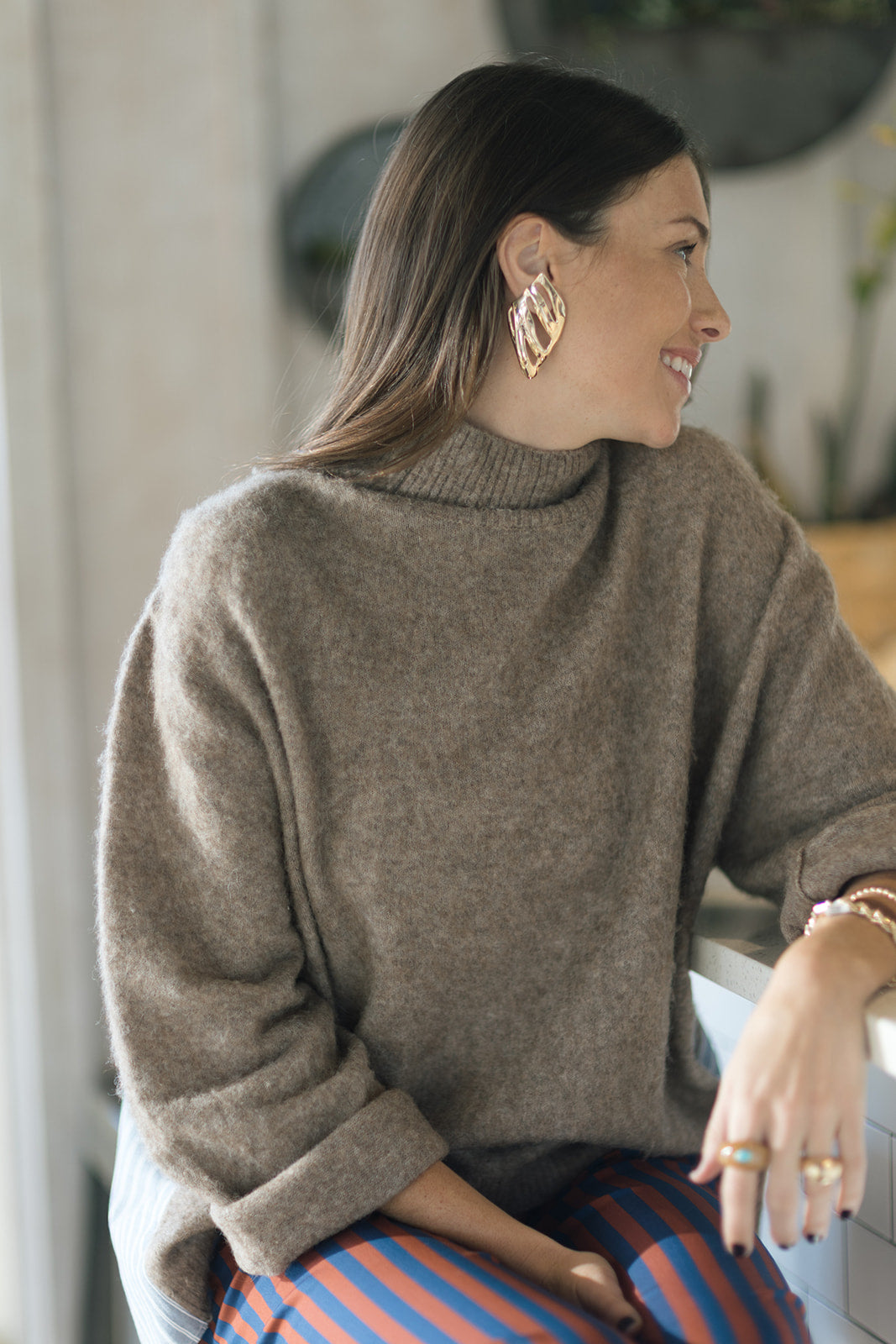Woman wearing a brown sweater and striped pants sitting indoors.