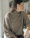 Woman wearing a brown sweater and striped pants sitting indoors.