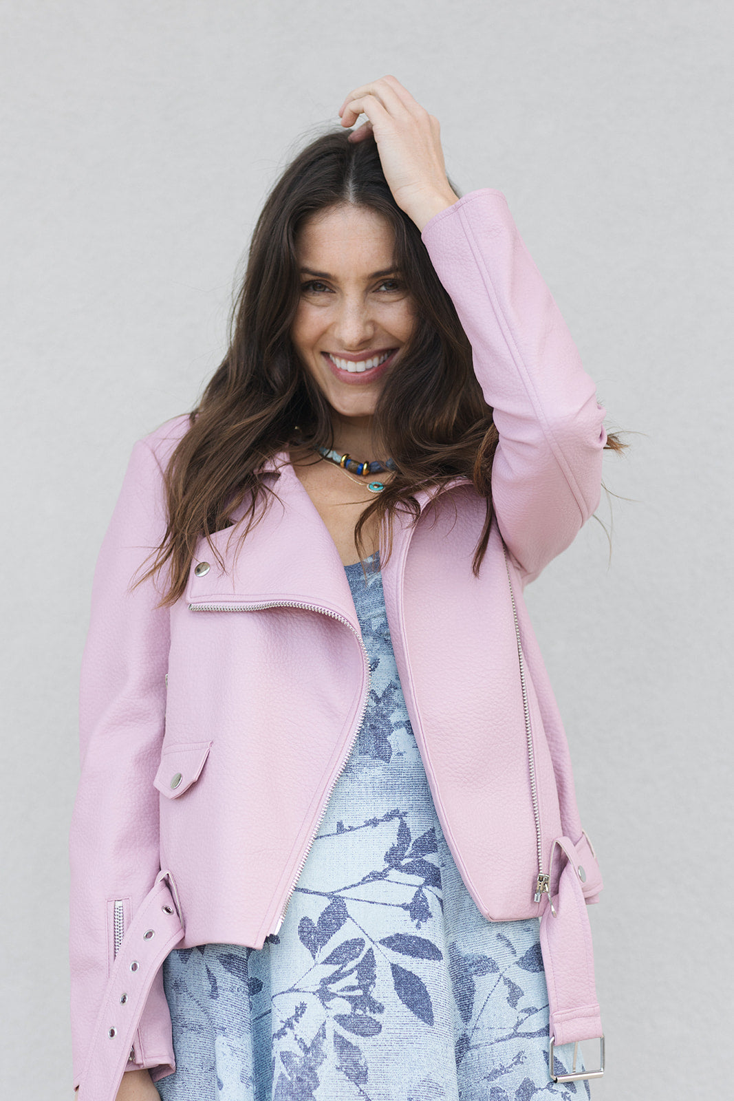 Woman wearing a pink coat over a floral dress against a plain background