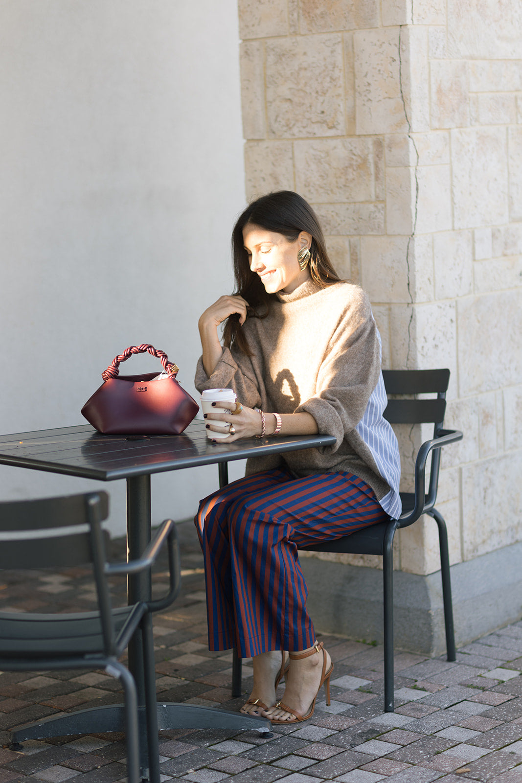 Woman sitting at an outdoor cafe table with a red handbag and a cup.