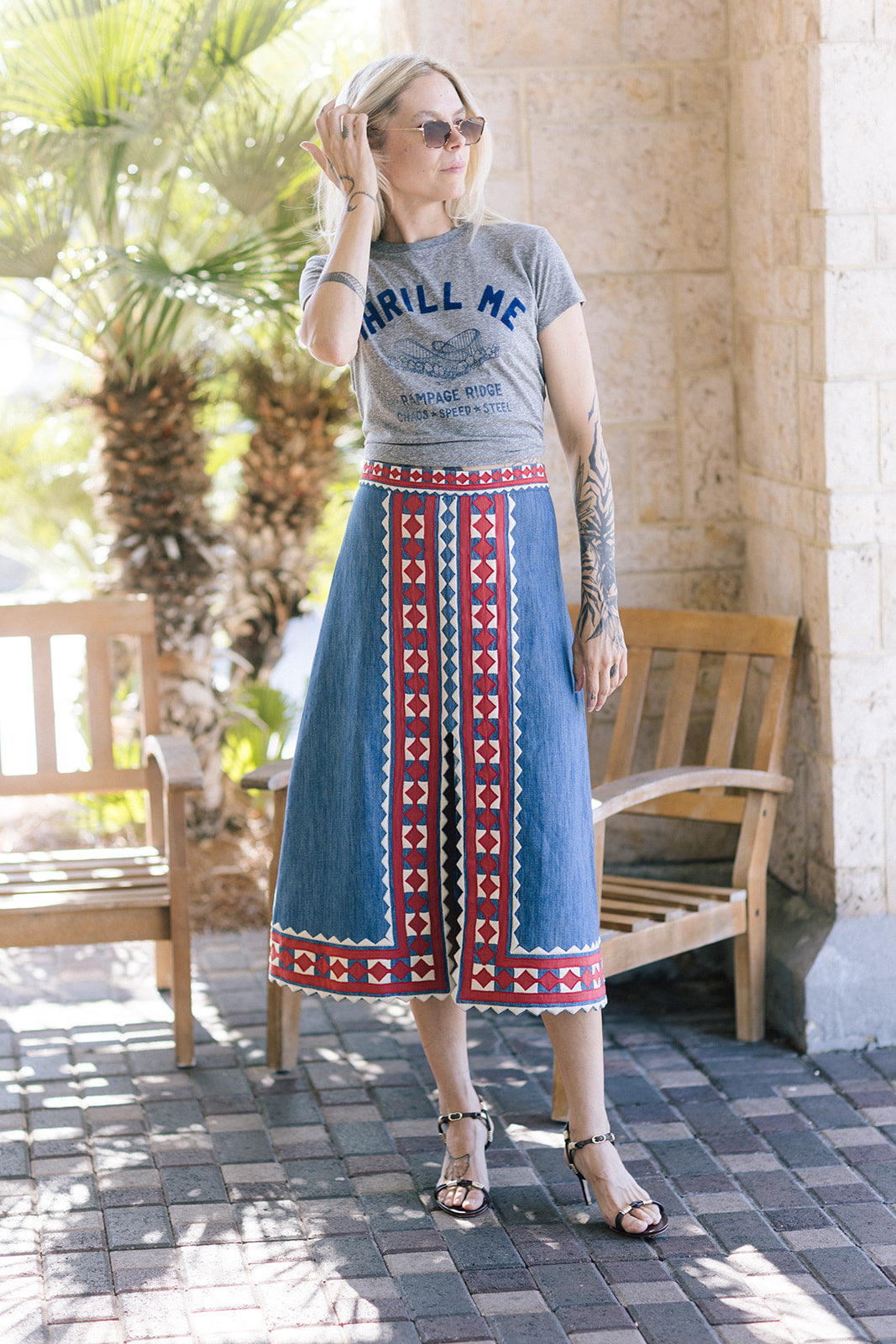 Woman wearing a graphic t-shirt and patterned skirt standing outdoors.
