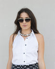 Woman wearing a white sleeveless shirt and polka dot skirt with sunglasses against a plain background