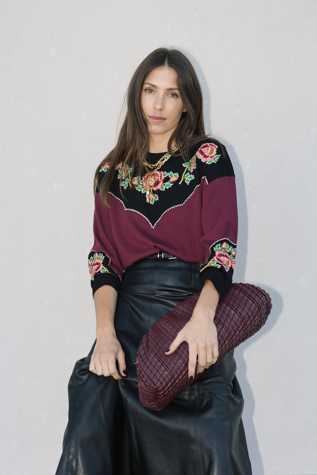 Woman wearing a black and purple embroidered top, holding vino bag with a plain background