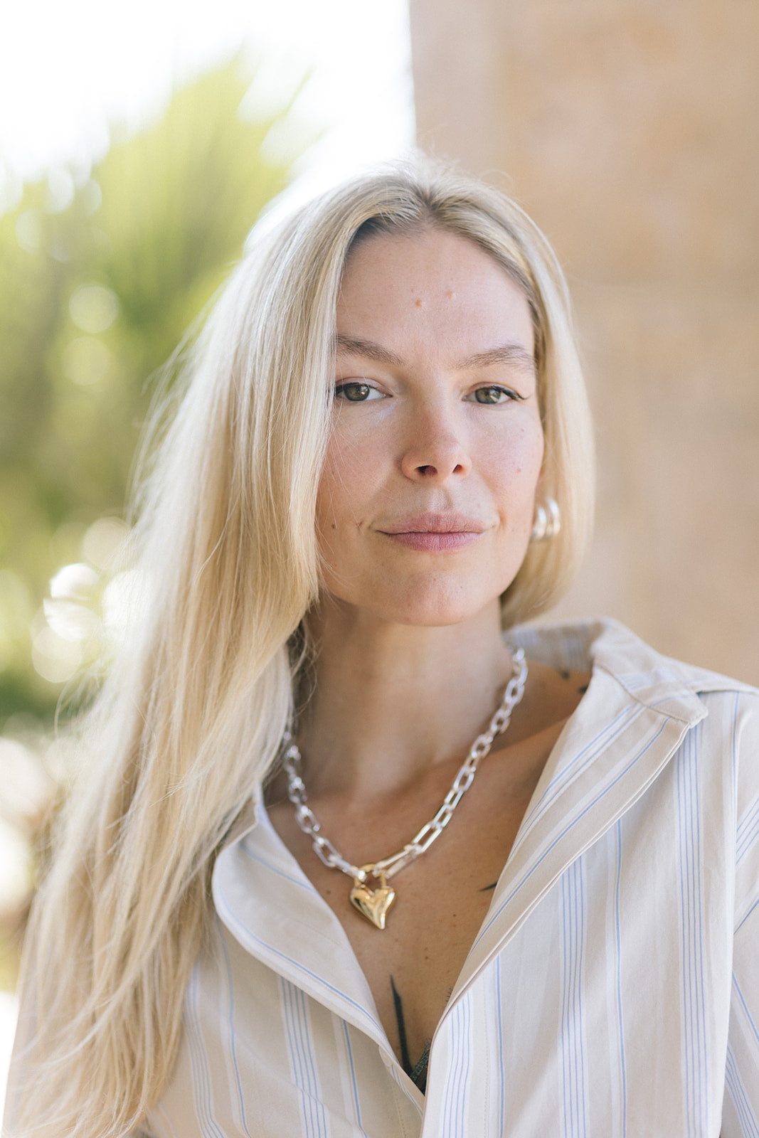 Woman with long blonde hair wearing a striped shirt and necklace outdoors