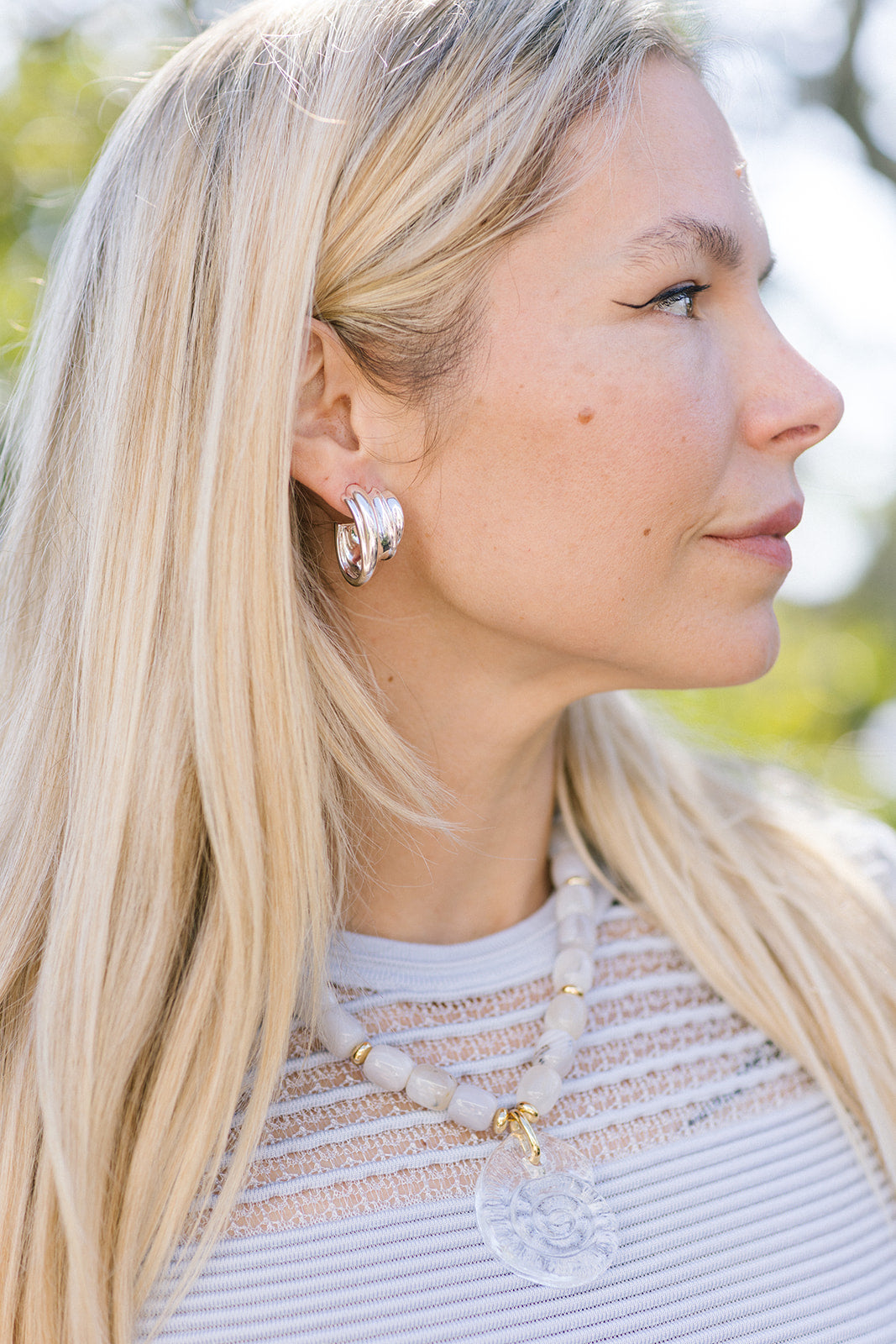 Close-up of a woman wearing Leona Hoops Silver and a necklace with a blurred natural background