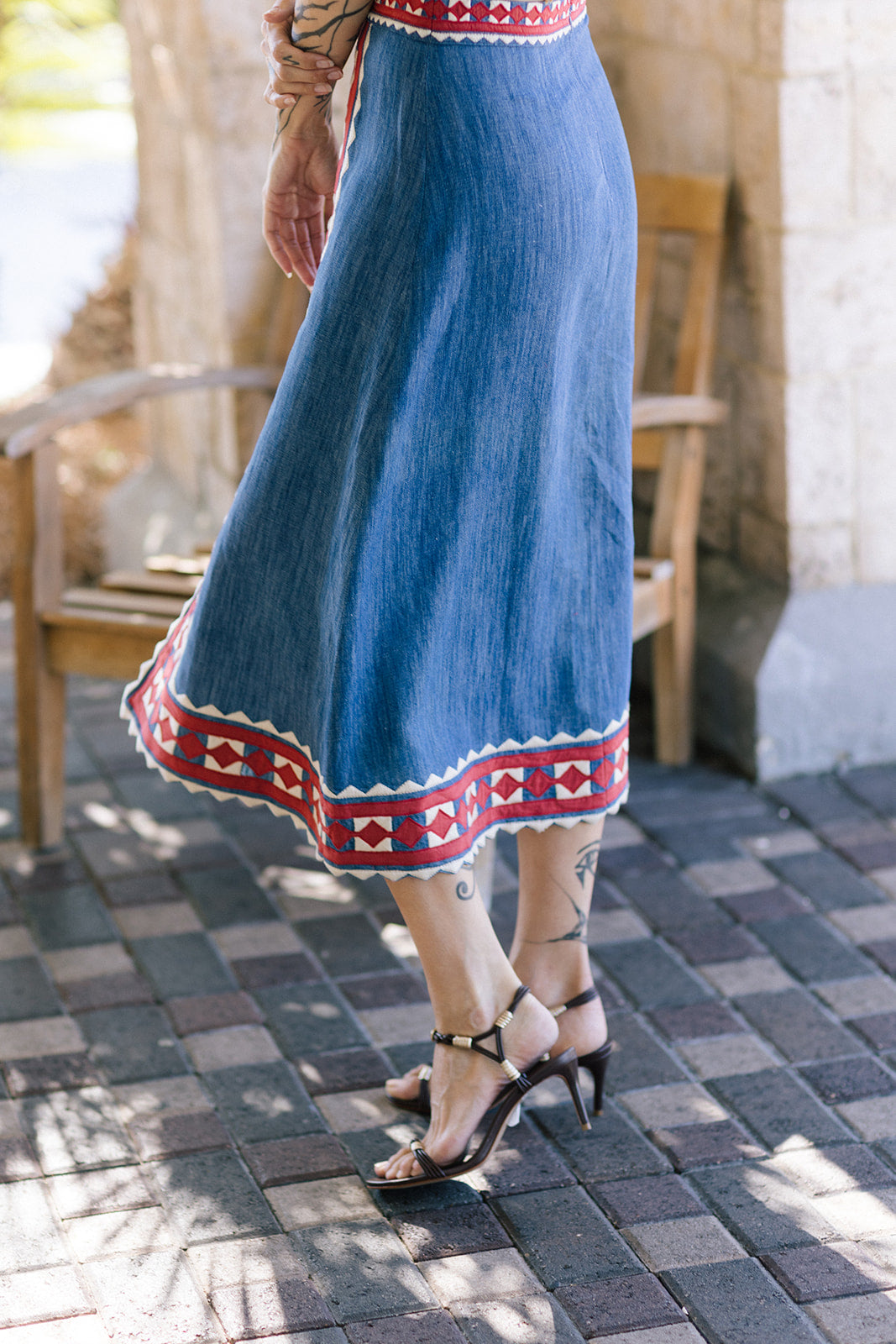 Person wearing a blue skirt with red and white pattern on a paved outdoor floor.