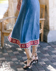 Person wearing a blue skirt with red and white pattern on a paved outdoor floor.