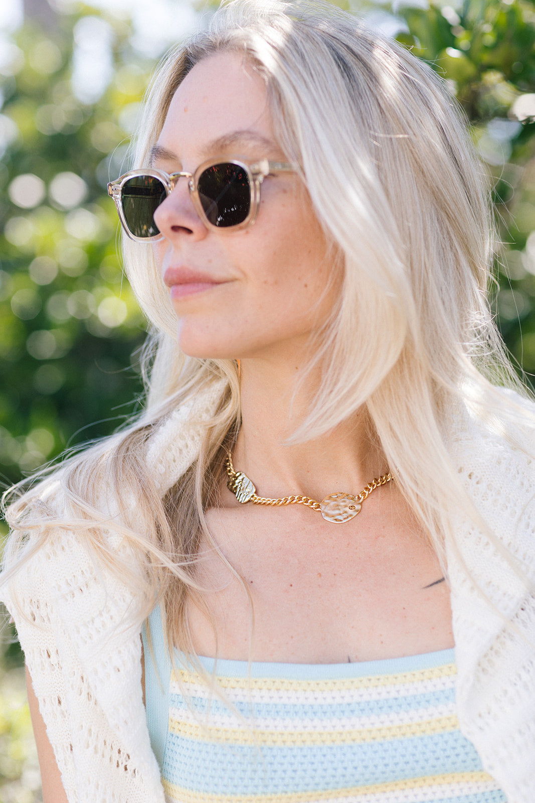 Woman wearing Campbell Haze 18k Polarized Sunglasses and a white cardigan with a blurred green background