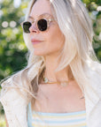 Woman wearing Campbell Haze 18k Polarized Sunglasses and a white cardigan with a blurred green background