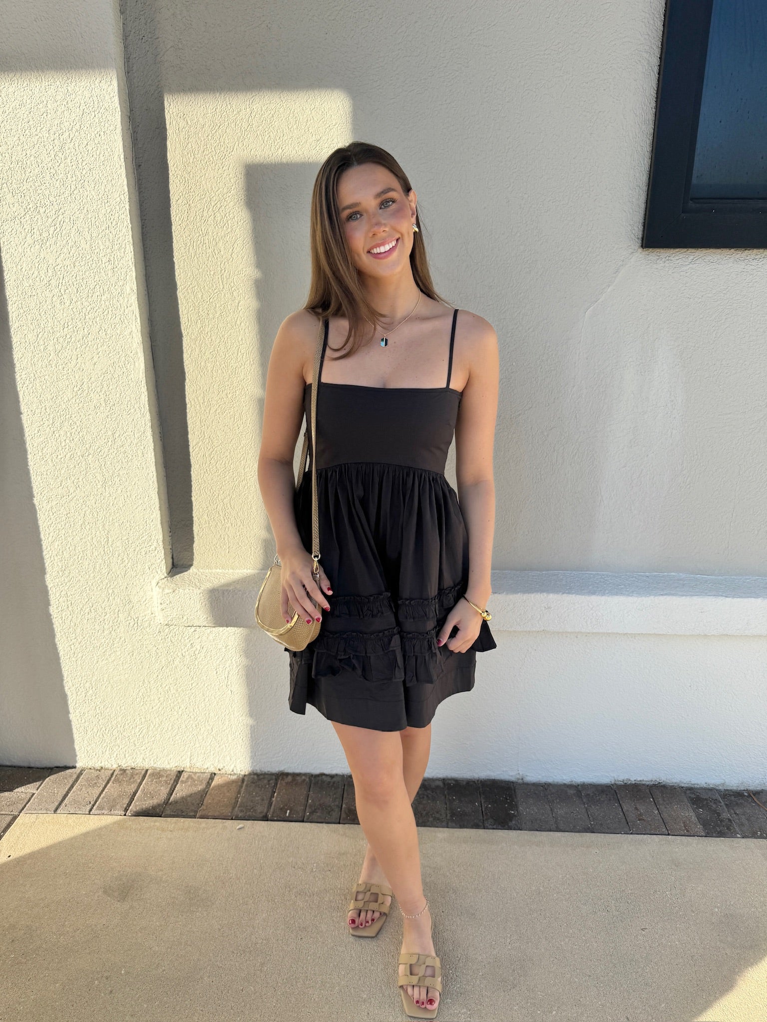 Woman in a black dress standing outdoors against a light-colored wall.