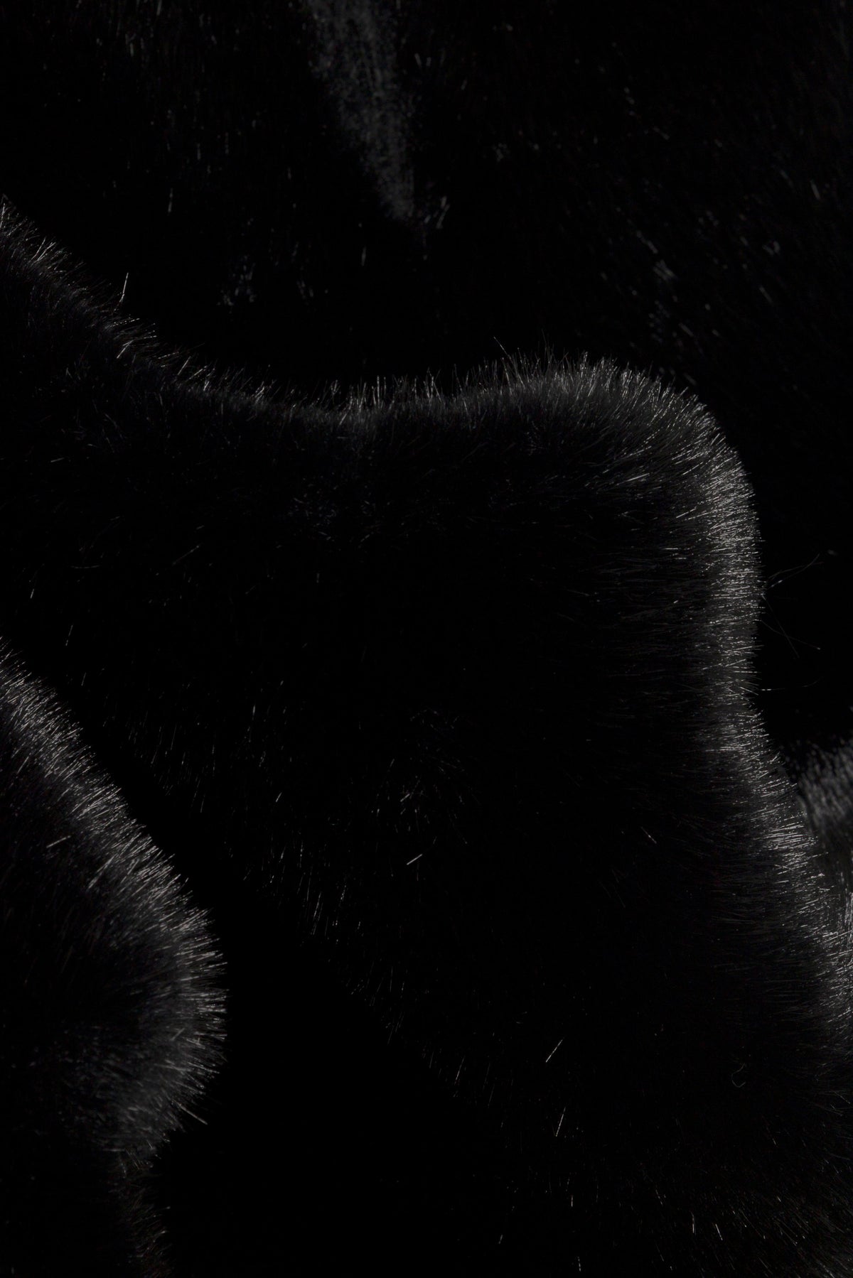 A close-up of black faux fur fabric with soft, textured strands and curved edges.