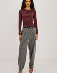model wearing a long sleeve merlot top with a cowl neck and grey pants on a light grey background 
