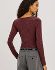 model wearing a long sleeve merlot top with a cowl neck and grey pants on a light grey background, back 