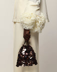 A close-up of a person wearing a cream-colored outfit with dramatic ruffled cuffs and holding Gala Bag in Dark Clove