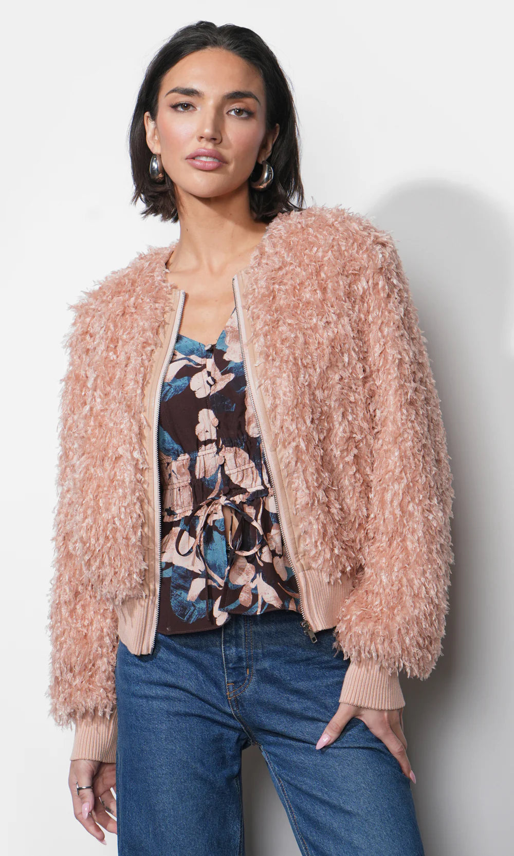 Woman wearing a fluffy pink jacket over a floral top and jeans on a plain background, open front