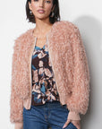 Woman wearing a fluffy pink jacket over a floral top and jeans on a plain background, open front