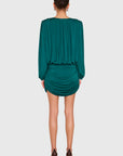 A woman shown from the back wearing a dark teal green draped mini dress with long sleeves and ruched detailing, paired with brown high heels, against a light gray studio background.