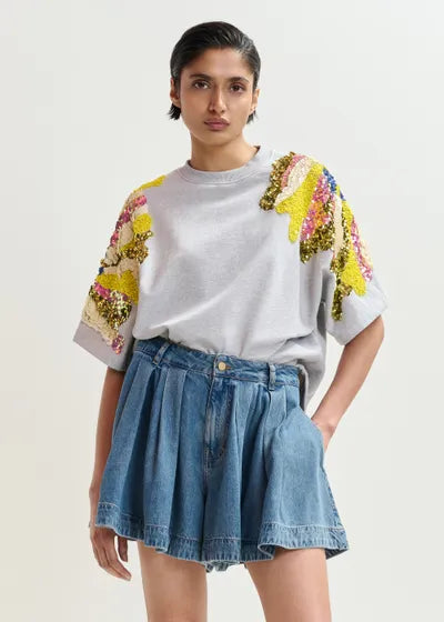Woman wearing a grey sweatshirt with colorful sleeves and a denim skirt on a light background