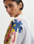 Woman wearing a gray sweatshirt with colorful sequin embellishments on the shoulders against a white background