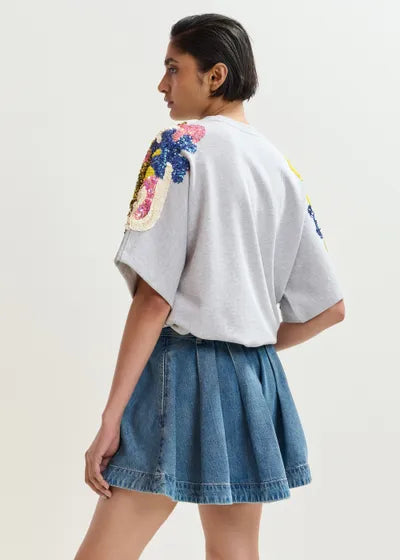 Woman wearing a gray t-shirt with floral designs on the back and a denim skirt against a white background