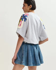Woman wearing a gray t-shirt with floral designs on the back and a denim skirt against a white background