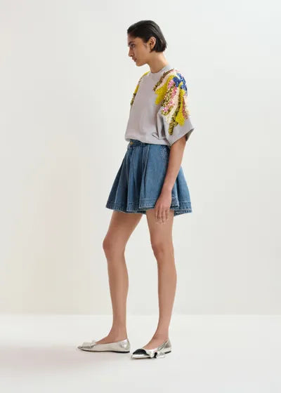 Woman wearing a floral embroidered top and denim skirt on a white background