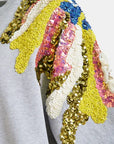 Colorful sequin headband with gold, pink, blue, and yellow patterns on a gray background.