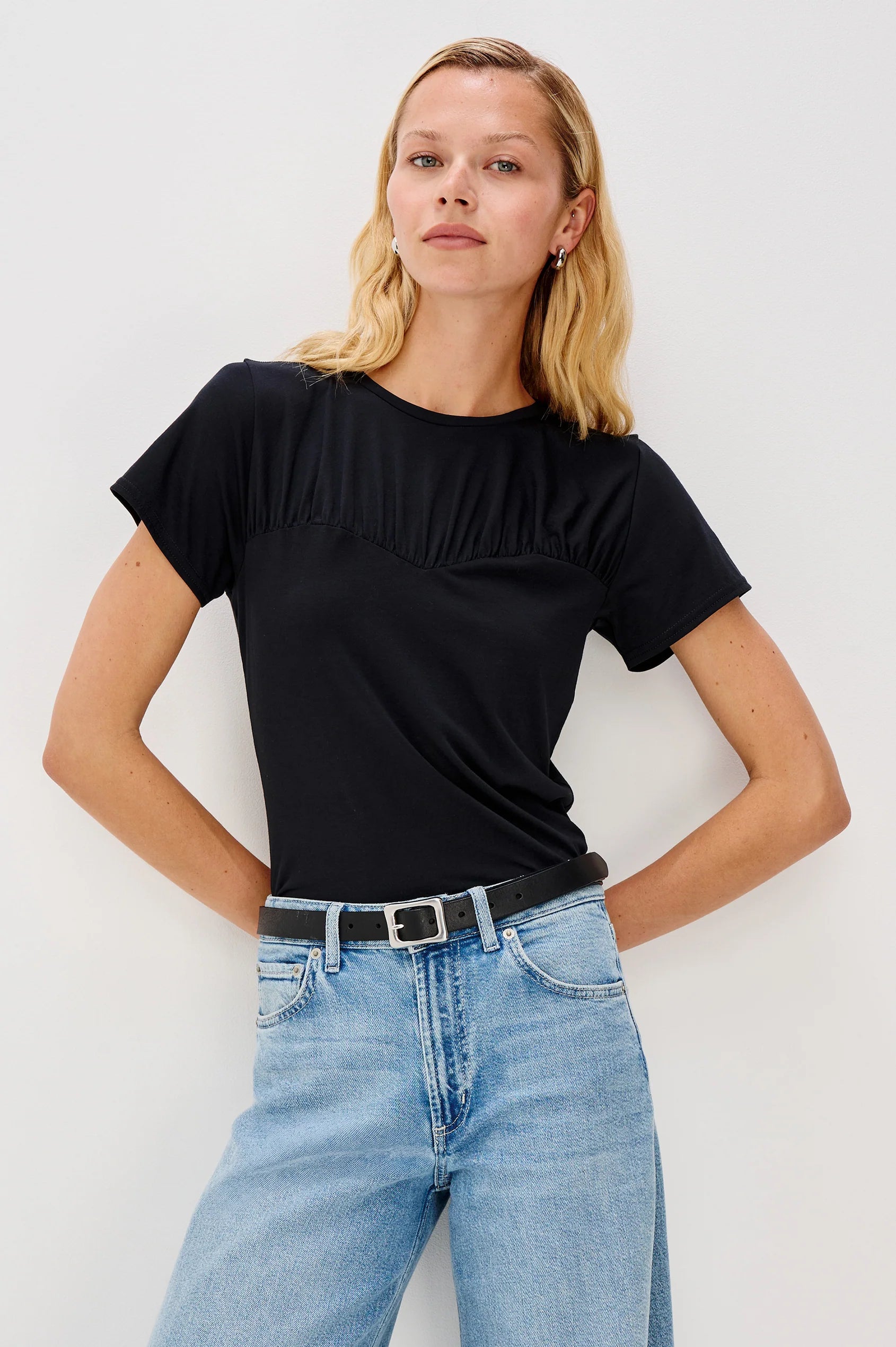 Woman wearing a black top and blue jeans against a white background front view
