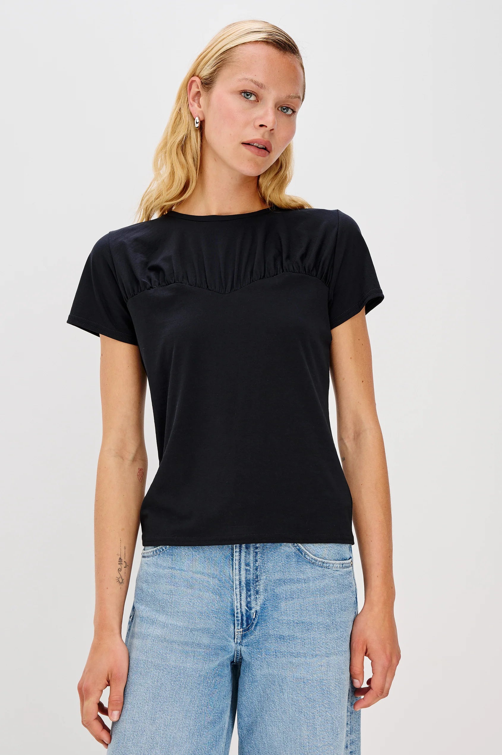 Woman wearing a black ruffled t-shirt and blue jeans on a white background front view