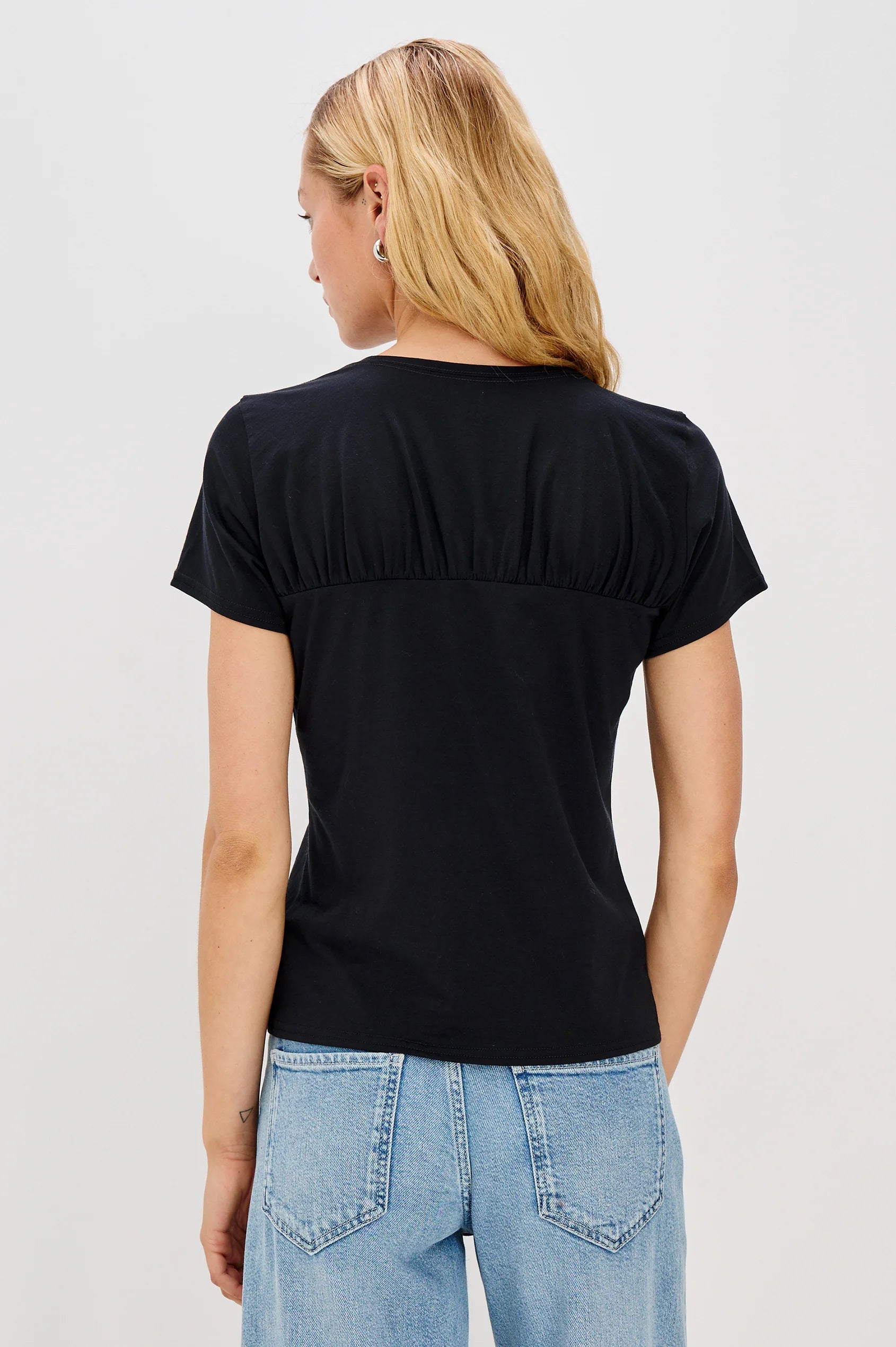 Person wearing a black t-shirt and light blue jeans on a plain background back view