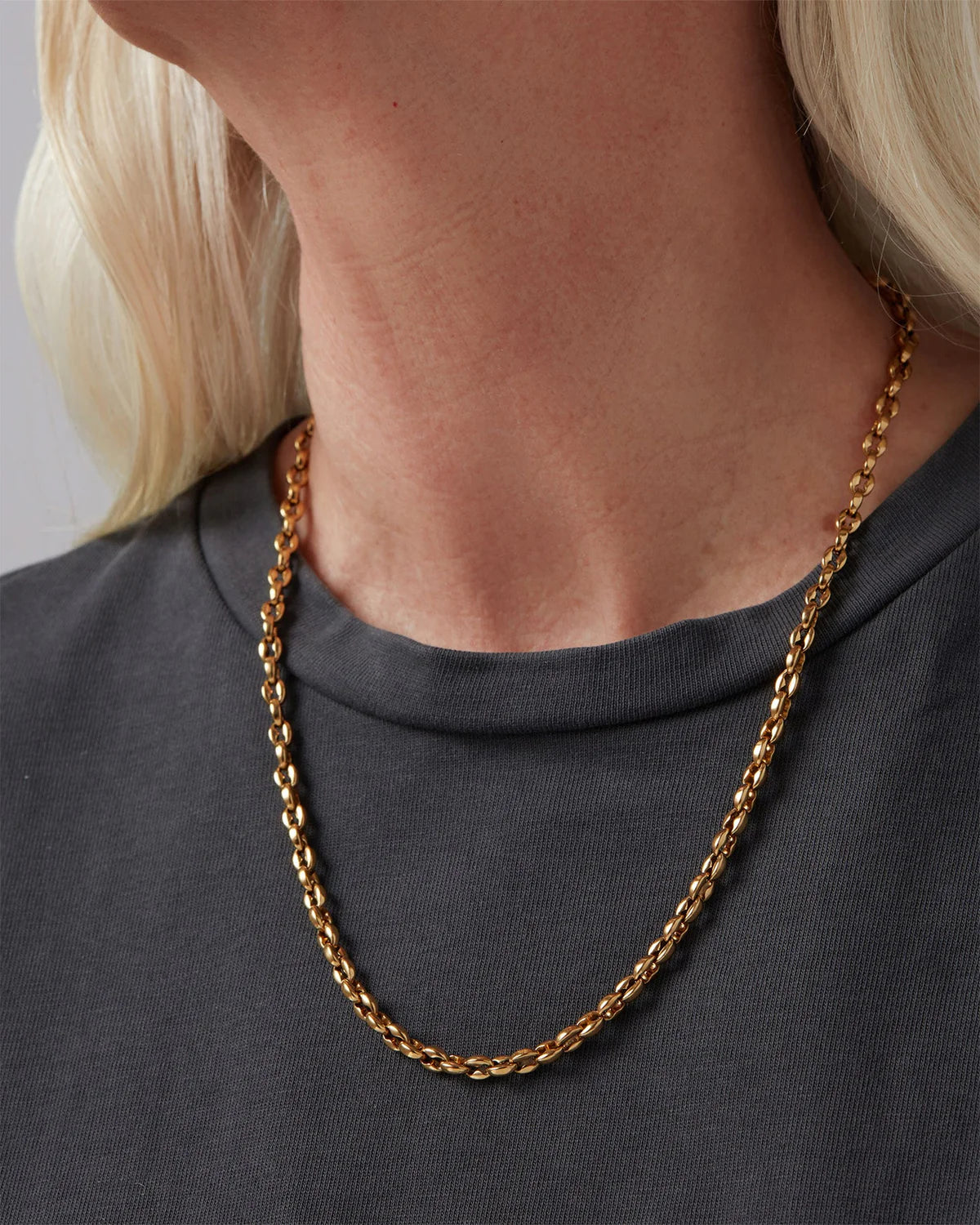 Gold chain necklace worn by a person with a neutral background