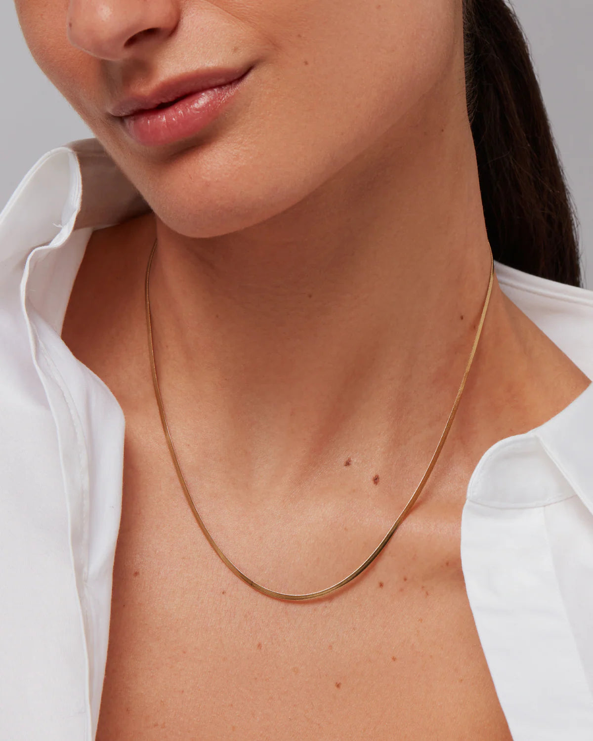 Close-up of a person wearing a gold necklace with a plain background
