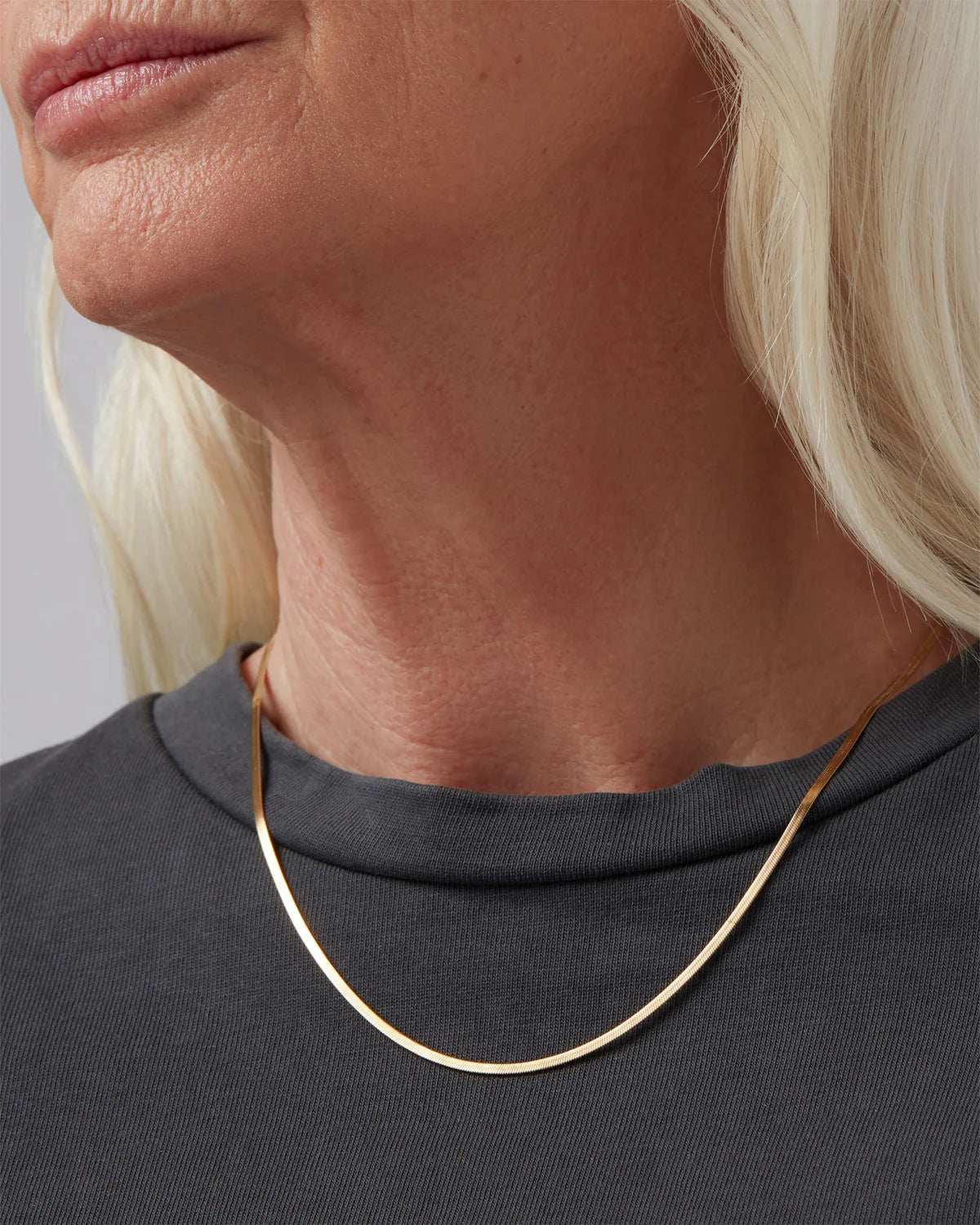 Close-up of a person wearing a thin gold necklace against a neutral background