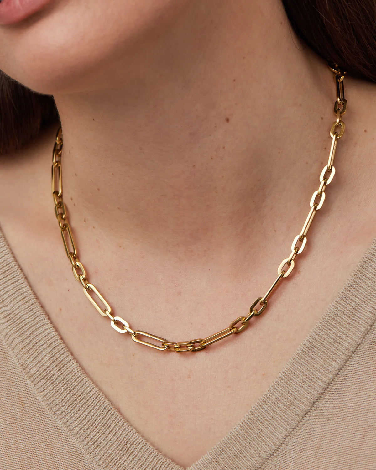 Gold chain necklace worn by a person with a neutral background