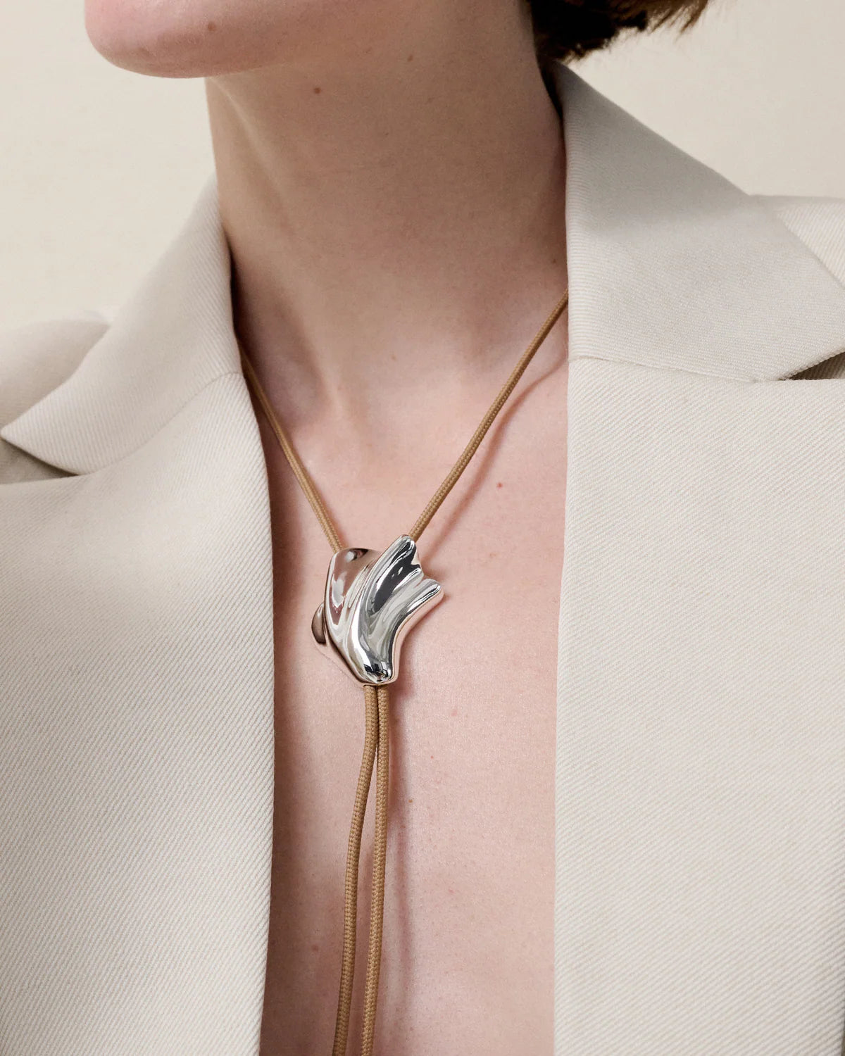 Necklace with a silver pendant worn by a person in a beige outfit