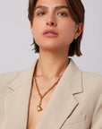 Woman wearing a beige blazer and gold necklace with a heart pendant on a plain background
