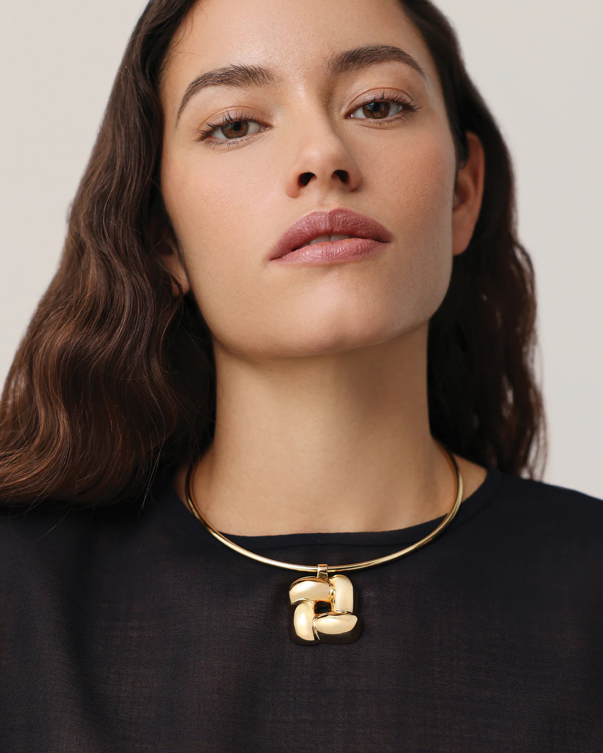 Woman wearing a gold necklace with a pendant against a neutral background