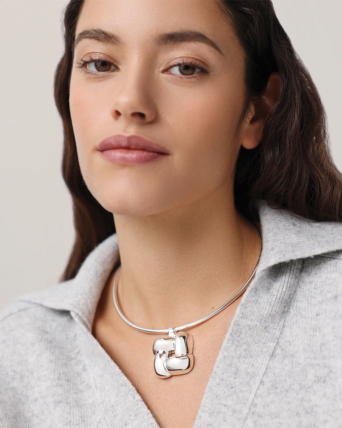 Woman wearing a silver necklace with a unique pendant against a neutral background