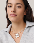 Woman wearing a silver necklace with a unique pendant against a neutral background