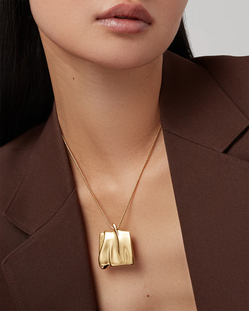 Gold necklace with a pendant worn by a person against a neutral background