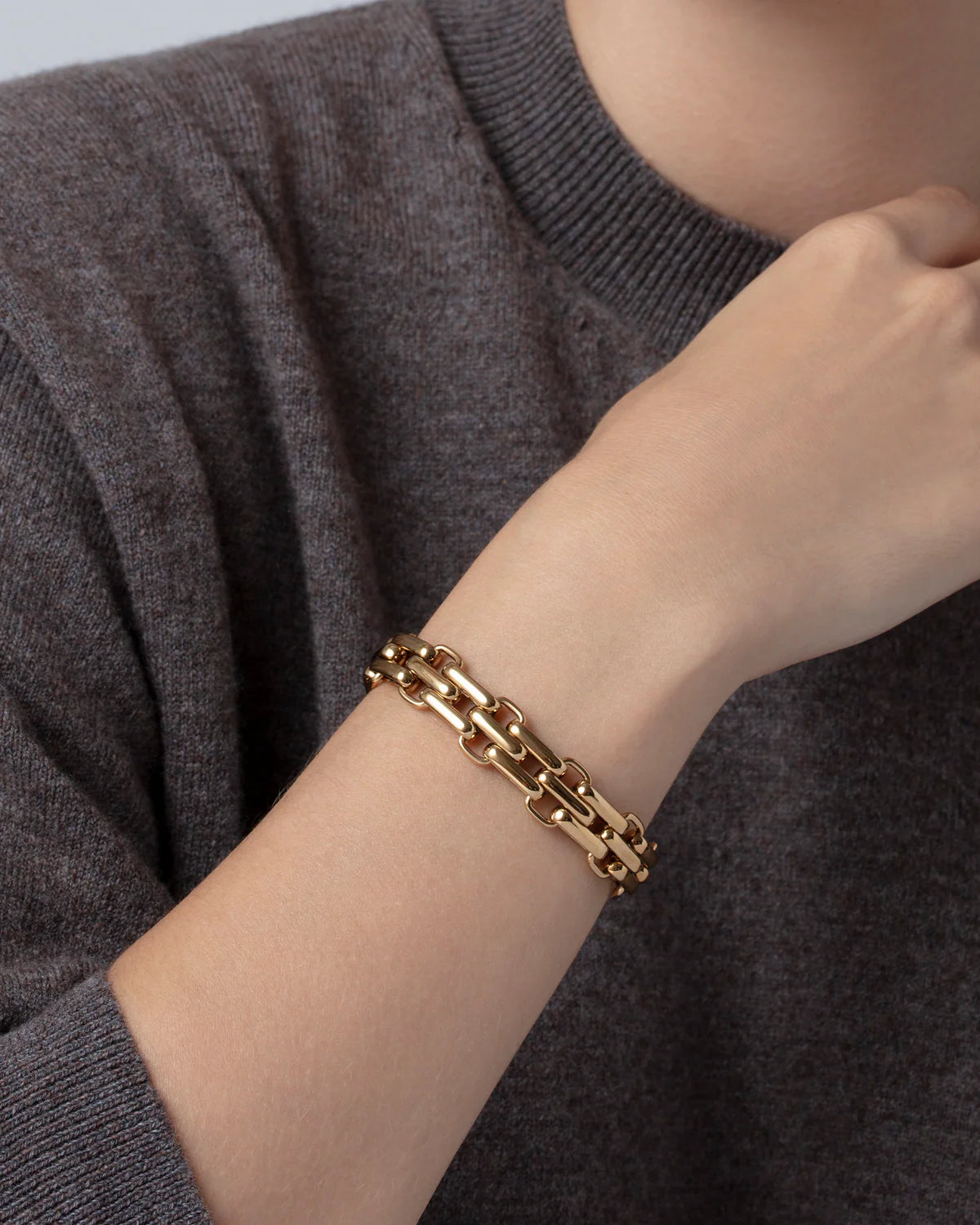 Gold chain bracelet on a wrist with a gray sweater background